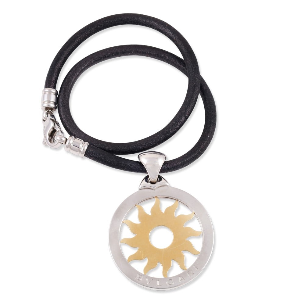 18KT GOLD AND STEEL SUN PENDANT SUSPENDED FROM A LEATHER CORD WITH STEEL CLASP, BY BULGARI: Pendant diameter approx. 4,3 cm Necklace length approx. 38,5 cm Pendant and clasp signed Bvlgari