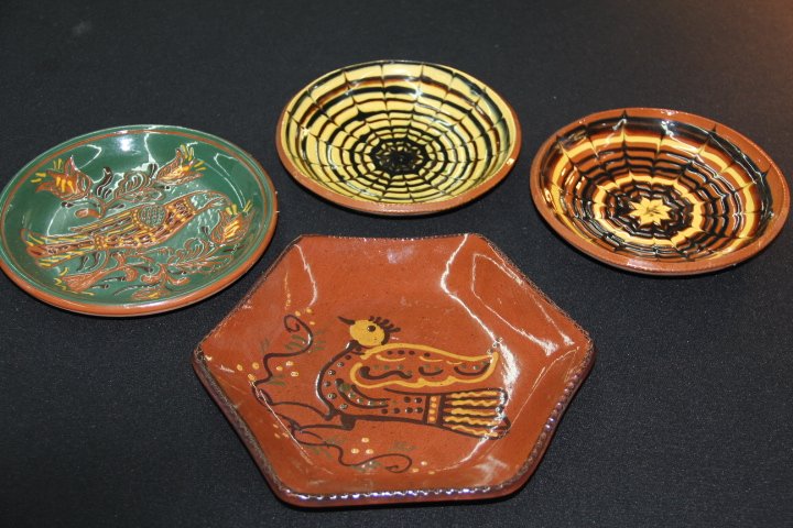 Four Redware Plates: 188-1742-1981 Four Redware plates. Three marked Nolde Forest and one marked Cazan. The brown plate with bird in center is Cazan. Sample of yellow spiral "It's a windy day", signed, from Village of Ang