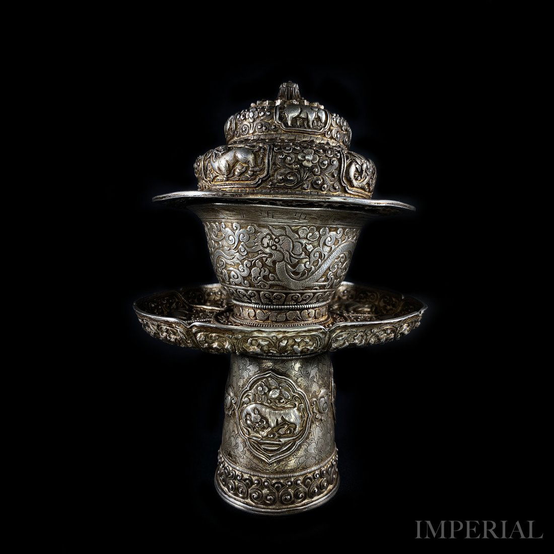 A FINE SILVER OFFERING CUP WITH STAND AND COVER, 1800s: A FINE SILVER REPOUSSÉ OFFERING CUP WITH STAND AND COVER, Tibet, 19th Century or earlier. The set is decorated with masterfully done repoussé dragons, other zodiac animals and many auspicious symbol