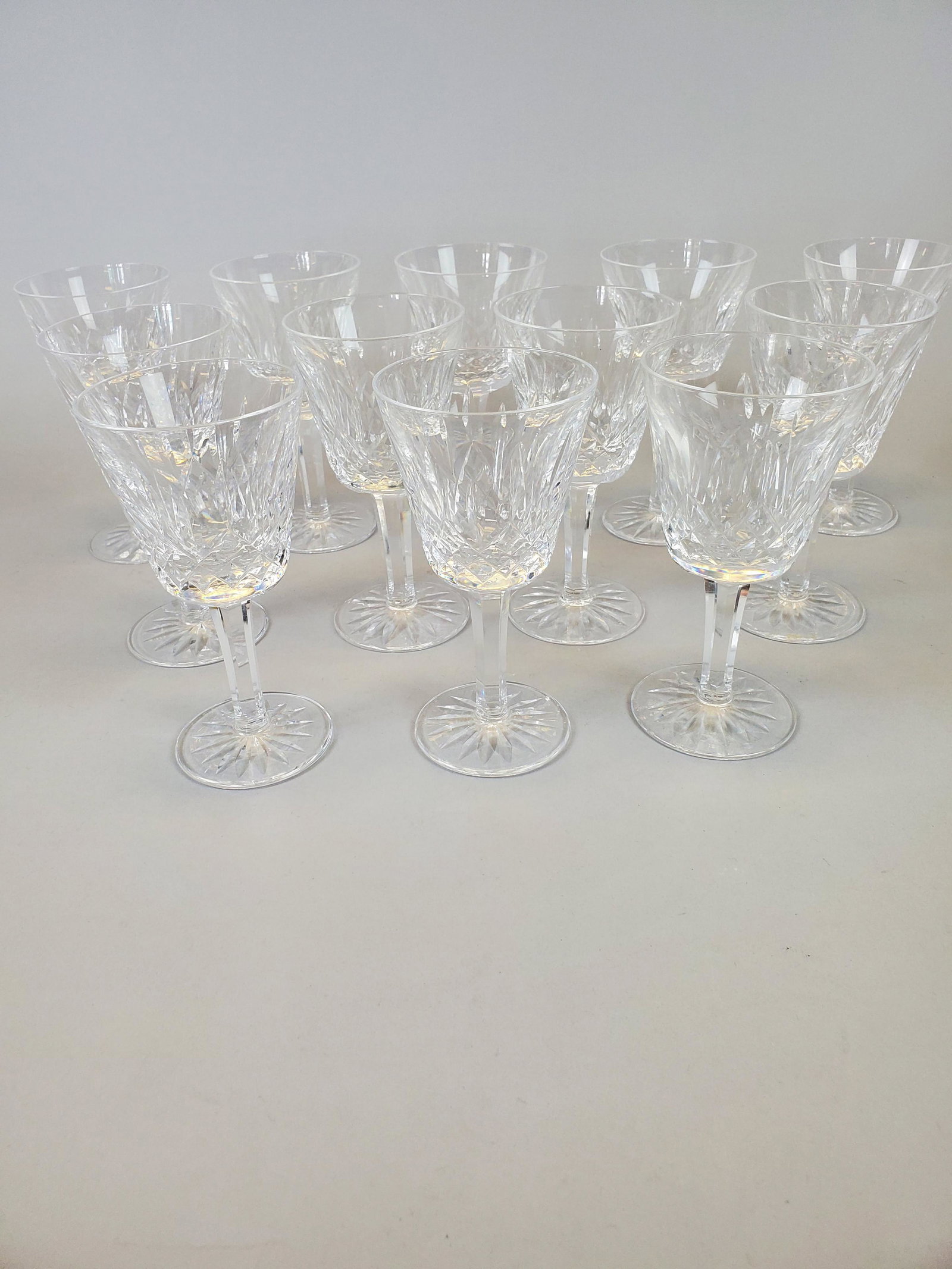 Twelve Waterford Lismore Crystal White Wine Glasses: Glasses from Waterford's classic 'Lismore' line. Each features Waterford manufacturer's watermark to bottom of foot. Small chip to rim of one glass, otherwise excellent with no other damage. Approxima