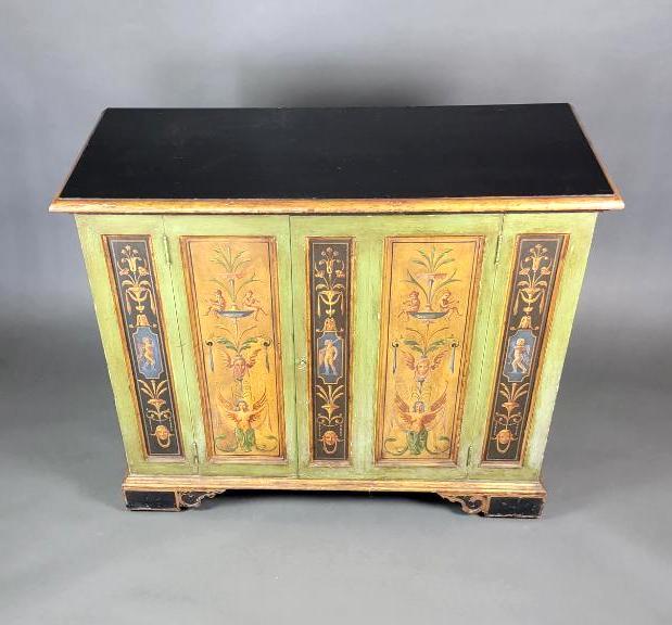 VTG 18th Century Style Hand-Painted Italian Cabinet: The solid hand carved two door cabinet, richly decorated and gilded with polychrome neoclassic vignettes of urns, swags, floral sprays, putti, winged faces and winged nude female figures, raised over 