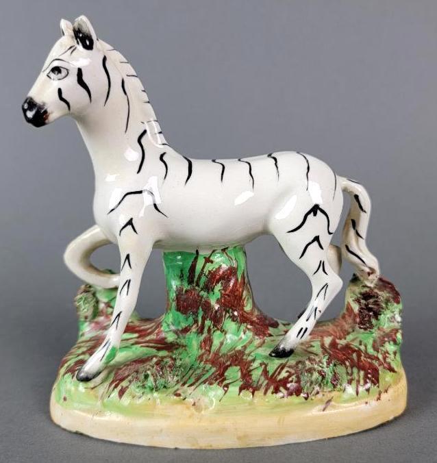 Antique Staffordshire Ceramic Porcelain Zebra Figure: The glazed pottery figurine representing the form of a zebra surmounting an ovular base decorated as a grassy knoll, the details hand painted, bottom with stamped 'Old Staffordshire Ware, England&