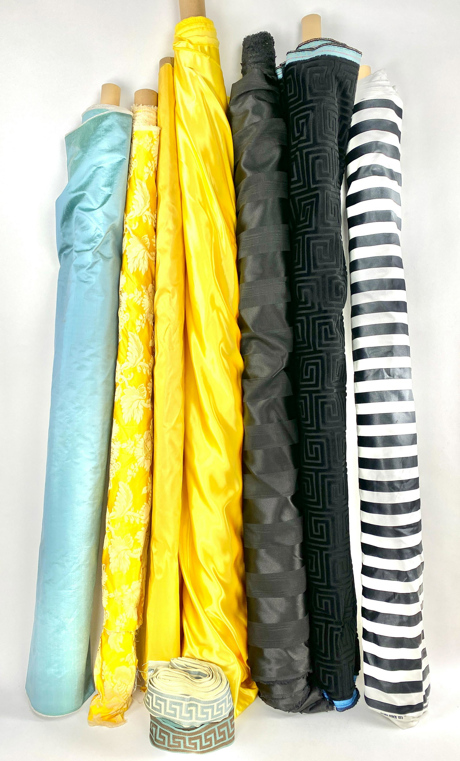 Bolts of Fabric and Trim: Bolts of fabric lined silk blue (27'.10" x 54"), yellow satin (60' x 60"), yellow silk (108" x 56"), yellow/gold and cream damask (56" x 45"), E.S.D black and white striped canvas (70" x 56"), and bla