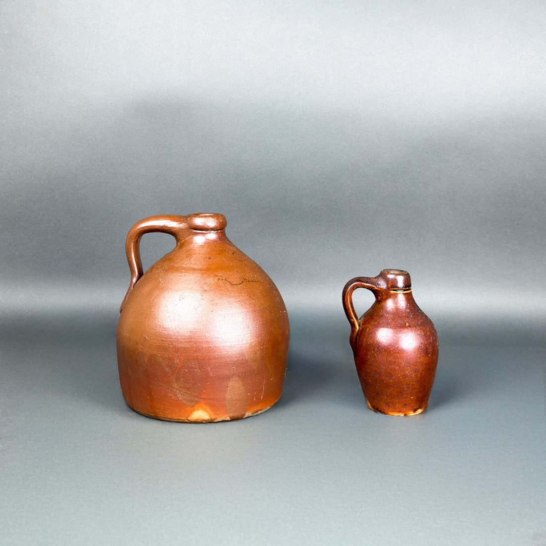 ANTIQUE STONEWARE JUGS WITH SLIP OR SALT GLAZES: Two antique stoneware jugs with bottle necks and finger handles in brown Albany slip glazes or salt glazes.