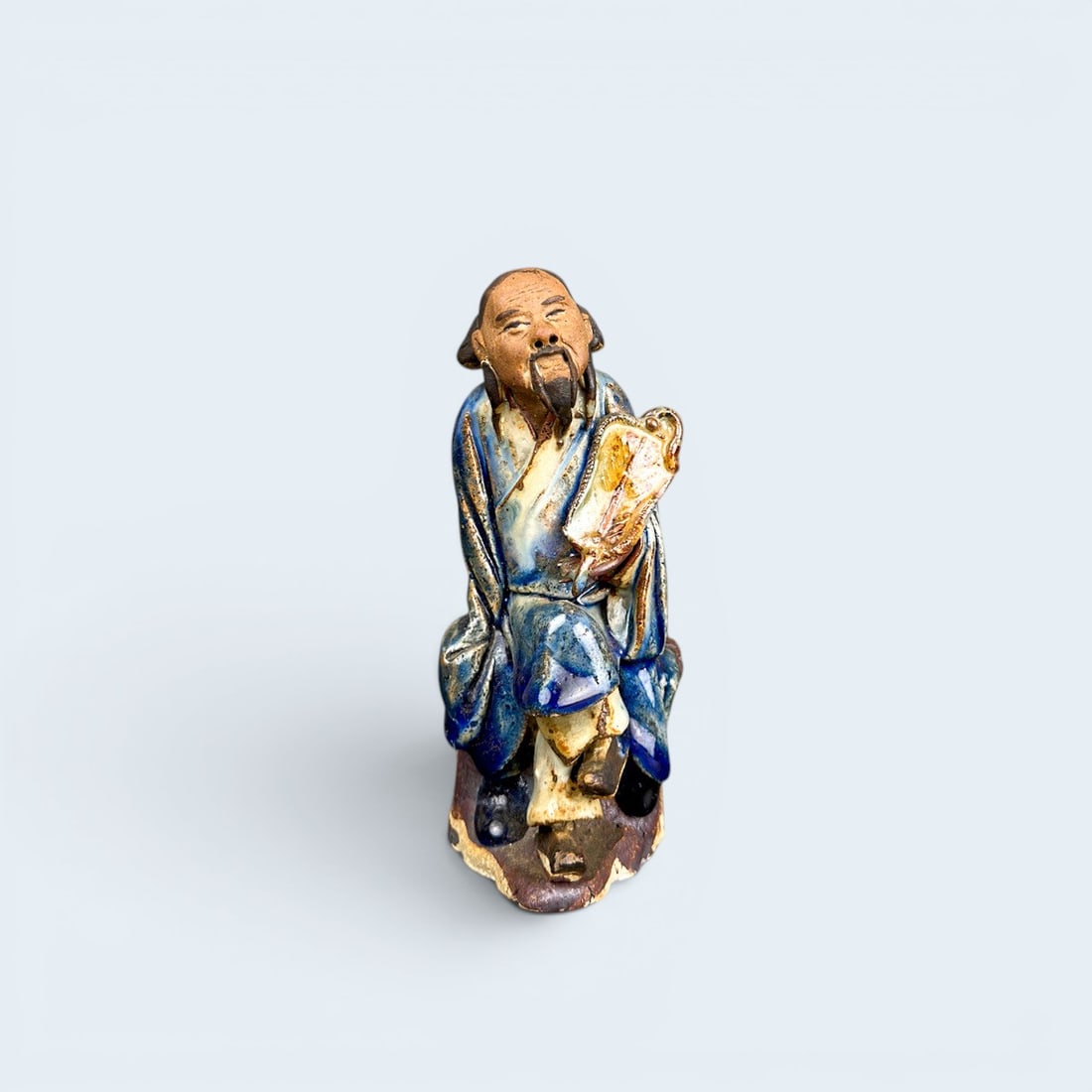 CHINESE MUD MAN FIGURINE: Antique chinese ceramic and glaze, mud man figurine holding fan with crossed legs. 5 1/2" h x 2 1/2" w x 2 3/4" d