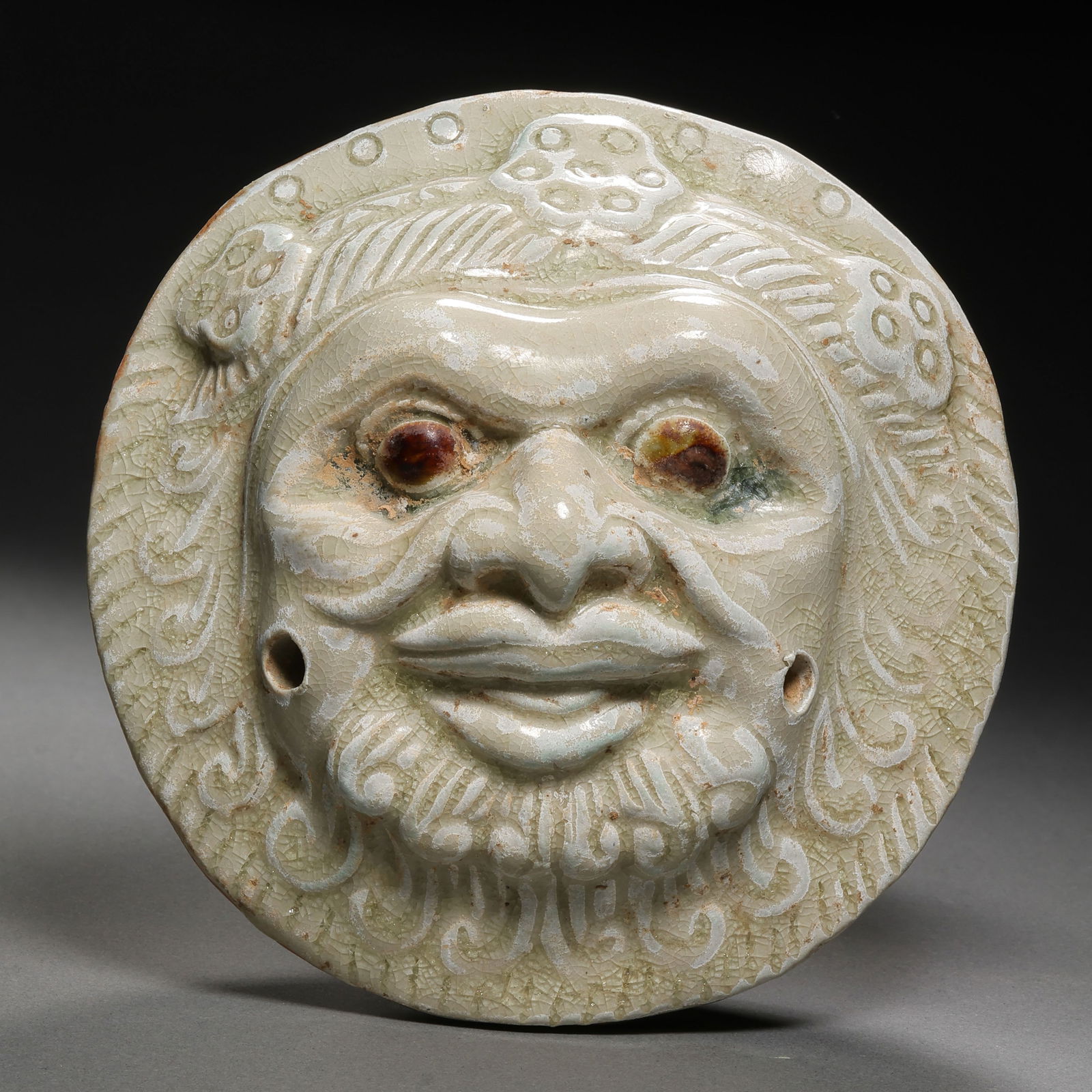 Chinese Sui Dynasty Xiangzhou Kiln celadon with brown-painted human face medallion: H. 6.5 cm. Diam. 13 cm.