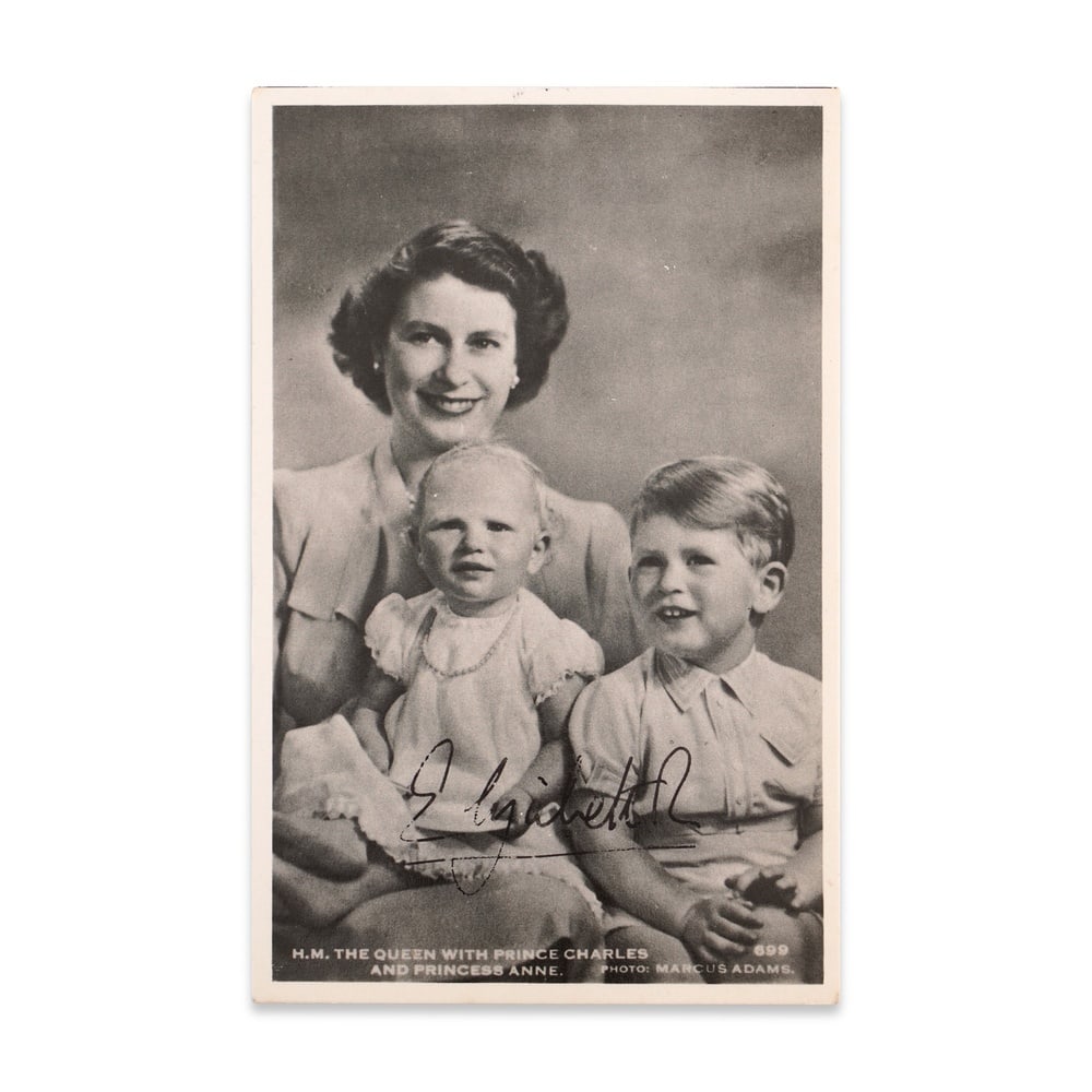 QUEEN ELIZABETH II SIGNED POSTCARD WITH PRINCE CHARLES AND PRINCESS ANNE: 5 1/2 x 3 1/2 in (14 x 8.8 cm) This vintage black-and-white postcard captures a tender family moment featuring the young Queen Elizabeth II with her two children-Prince Charles and Princess Anne.