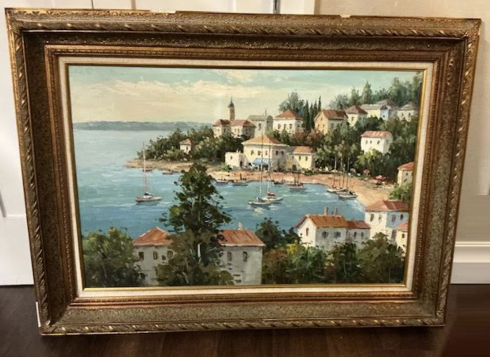 Wooden Framed Oil Painting On Canvas Depicting a coastal Mediterranean-style town with boats in the: Wooden Framed oil painting depicting a coastal Mediterranean-style town with boats in the harbor. . Canvas is 36 inches x 24 inches highWooden framease some top paint mark and sligh chipsFrame measure