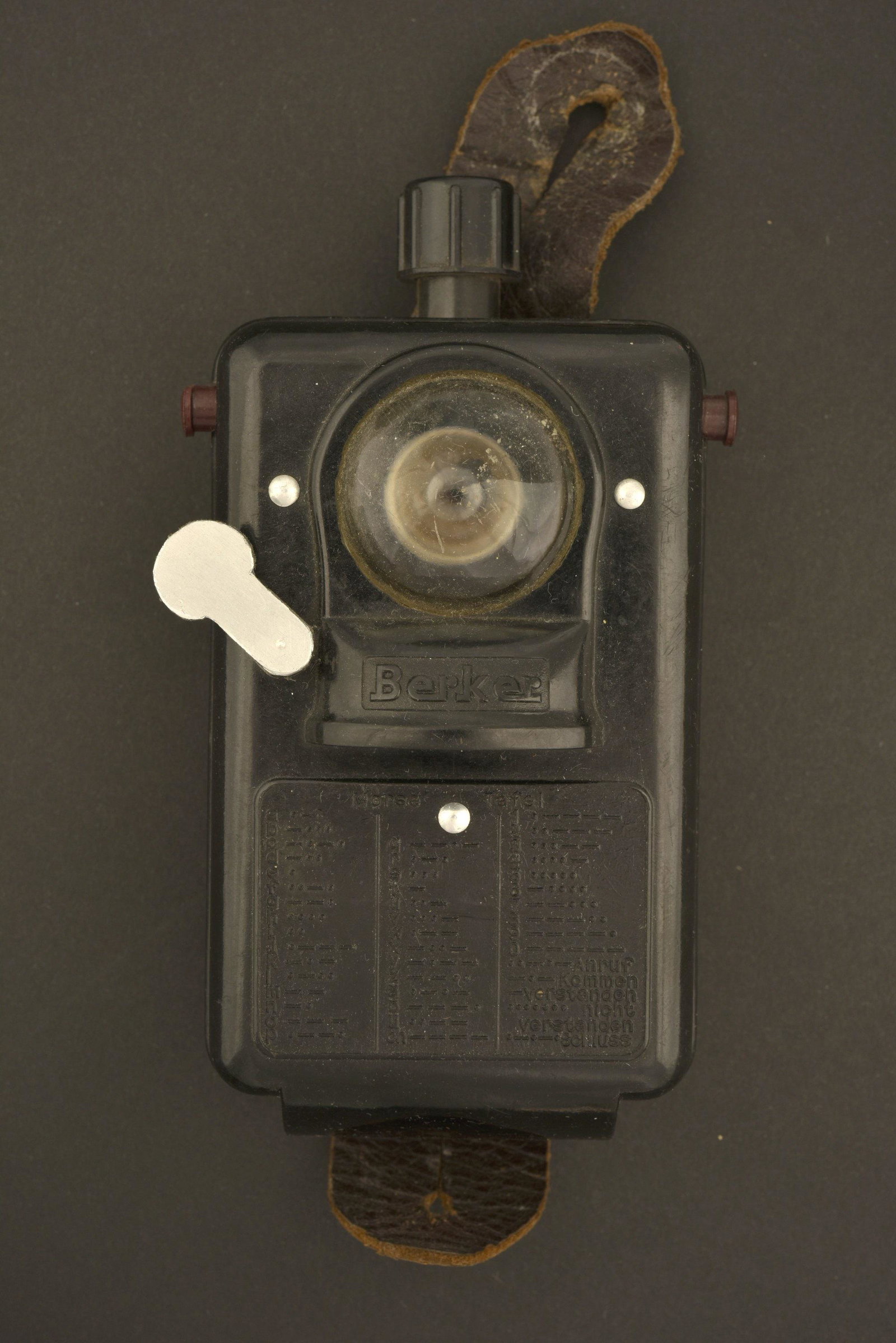 Lampe de poche Berker. Berker Flashlight: En bakelite noir, toutes les pieces mobiles sont fonctionnelles. Beau marquage Berker, notice d'utilisation morse moulee dans le bakelite. Ampoule presente. Patte en cuir complete. Pile manquante. A n