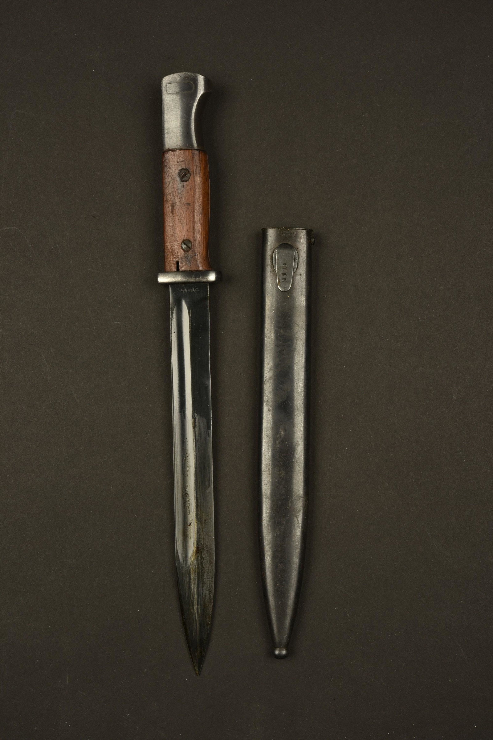 Baionnette 98K. 98K Bayonet: Plaquettes en bois verni, maintenues par deux rivets. Lame dans sa couleur d'origine a 98%, fabrication 41 CLC, numero 3093a. Garde portant le numero 7729. Fourreau en metal, peinture Ã 80%, numero