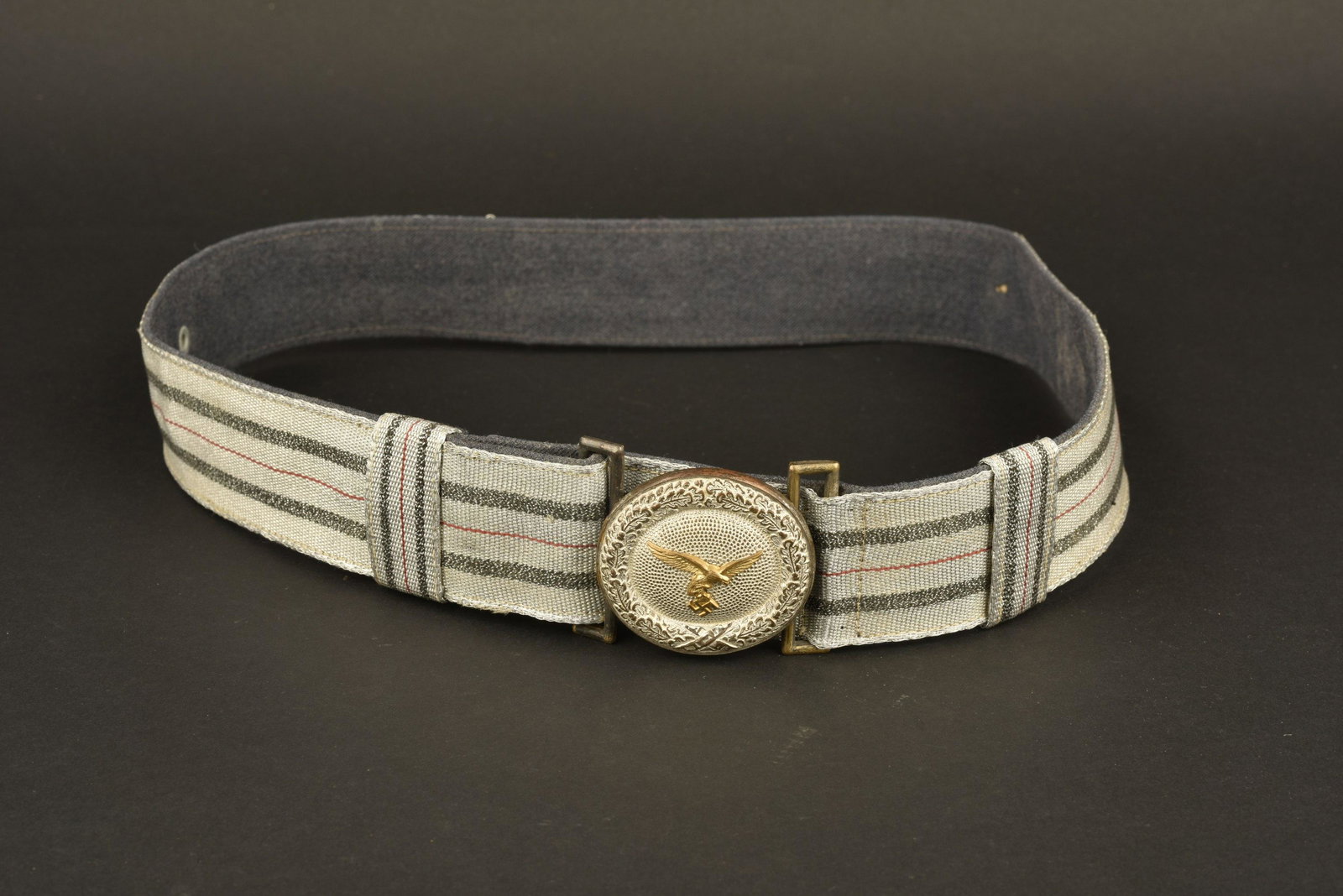 feldbinde officier LW. LW officer brocade: Ceinturon en fil argent et gris/bleu, lisere rouge au centre. Doublure en drap Feldgrau. Bouclerie complete. Boucle ronde, aigle de la Luftwaffe du 1er type rapporte, en metal dore. A noter une certai