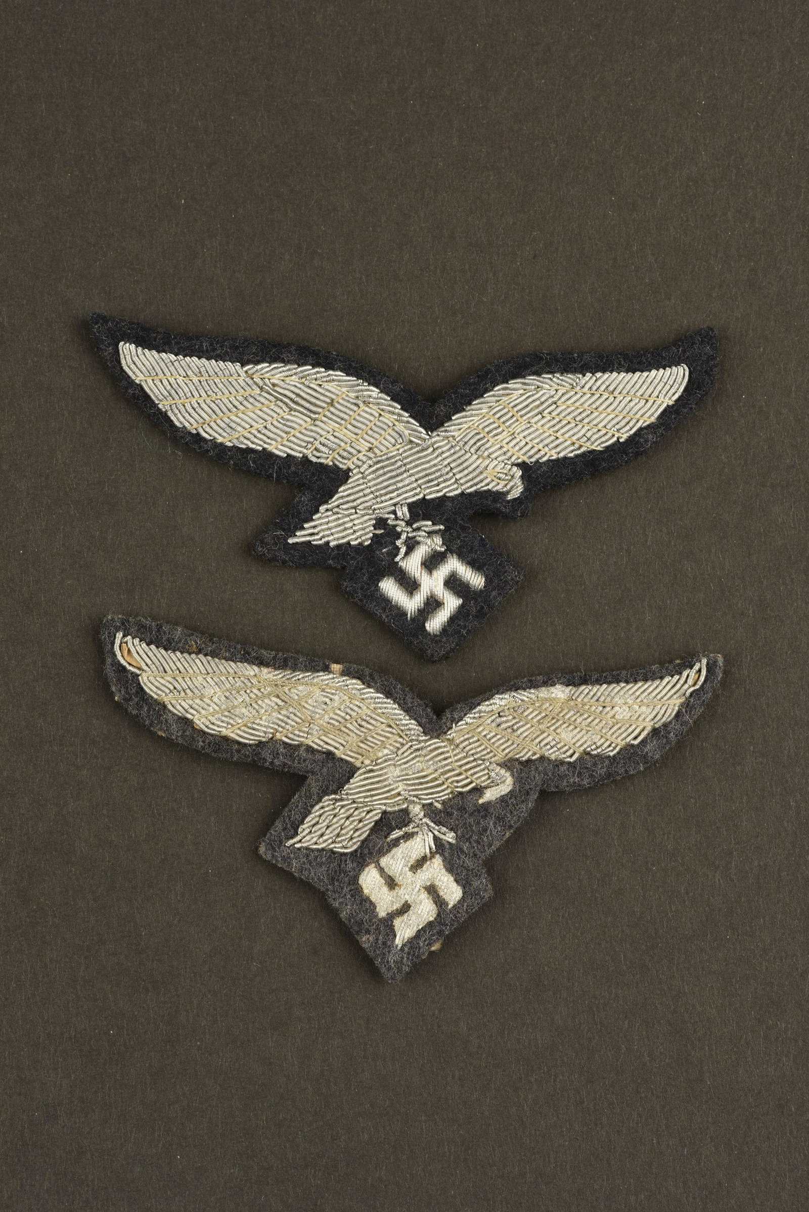 Aigles de poitrine officier LW. Officer LW eagles: Deux modeles differents d'aigles de poitrine en cannetille argent, sur fond gris/bleu. Aigles du second type. Jamais montes. A noter une legere usure des pieces. Un aigle presentant quelques traces d'