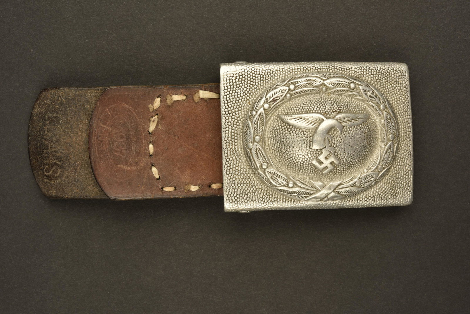 Boucle de ceinturon de la Luftwaffe. Luftwaffe belt: Boucle en aluminium grenelÃ©, aigle de la Luftwaffe du premier type. Patte en cuir prÃ©sente, couture refaite. Marquages LBAS 1937. A noter une certaine usure et patine de la piÃ¨ce. Grained alu