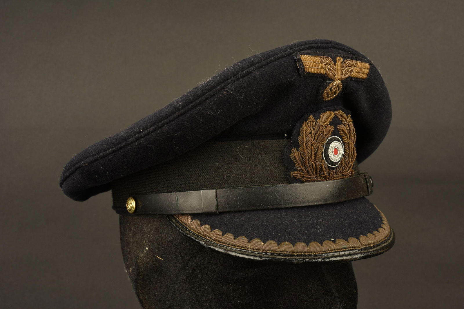 Kriegsmarine officer cap. Casquette officier KM: En drap bleu marine. Les insignes sont en cannetille, et visiblement montes main. Fausse jugulaire presente. Visiere en cuir double d'un drap bleu marine et d'une rangee de feuilles en cannetille or.