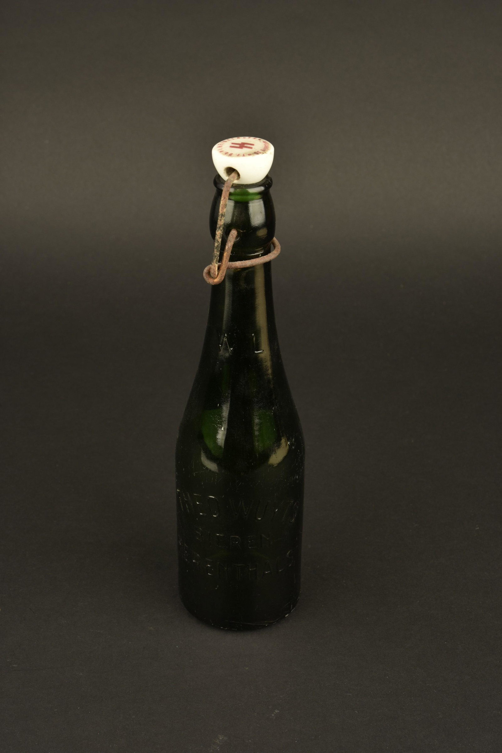 Bouteille de biere de la Waffen SS. SS bier bottle: Bouteille en verre vert. Marquee Theo Wuyts Bieren Herenthals. Bouchon complet, partie metallique oxydee. Marque SS sous forme runique. Fabrication SS Eigentum. Hauteur 25 cm. A noter une certaine usu