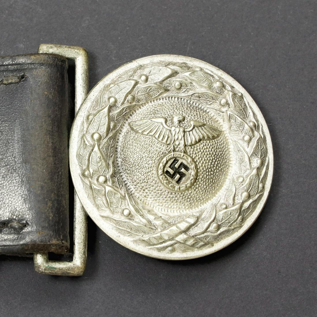 Ceinturon officier DLV. DLV officer belt: Ceinturon en cuir noir, les passants sont prÃ©sents. Patte de rÃ©glage complÃ¨te. Trace d'une doublure en feutrine. Boucle de ceinturon en mÃ©tal argentÃ©, sans marquages visibles. A noter u