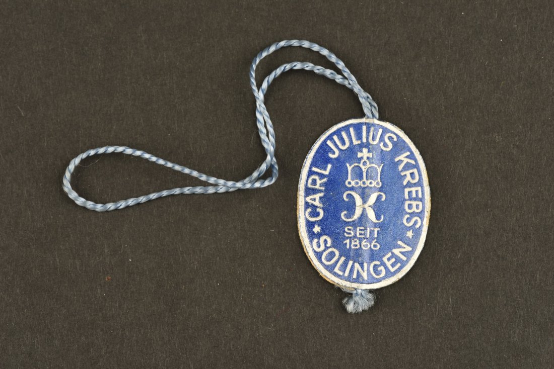 Etiquette de fabricant pour dague. Manufacturer: Etiquette de forme ovale en Ã©pais papier, couleur bleue, marquÃ©e Carl Julius Krebs Solingen, cordelette de fixation prÃ©sente. A noter une lÃ©gÃ¨re usure et patine de la piÃ¨ce. Oval-sha