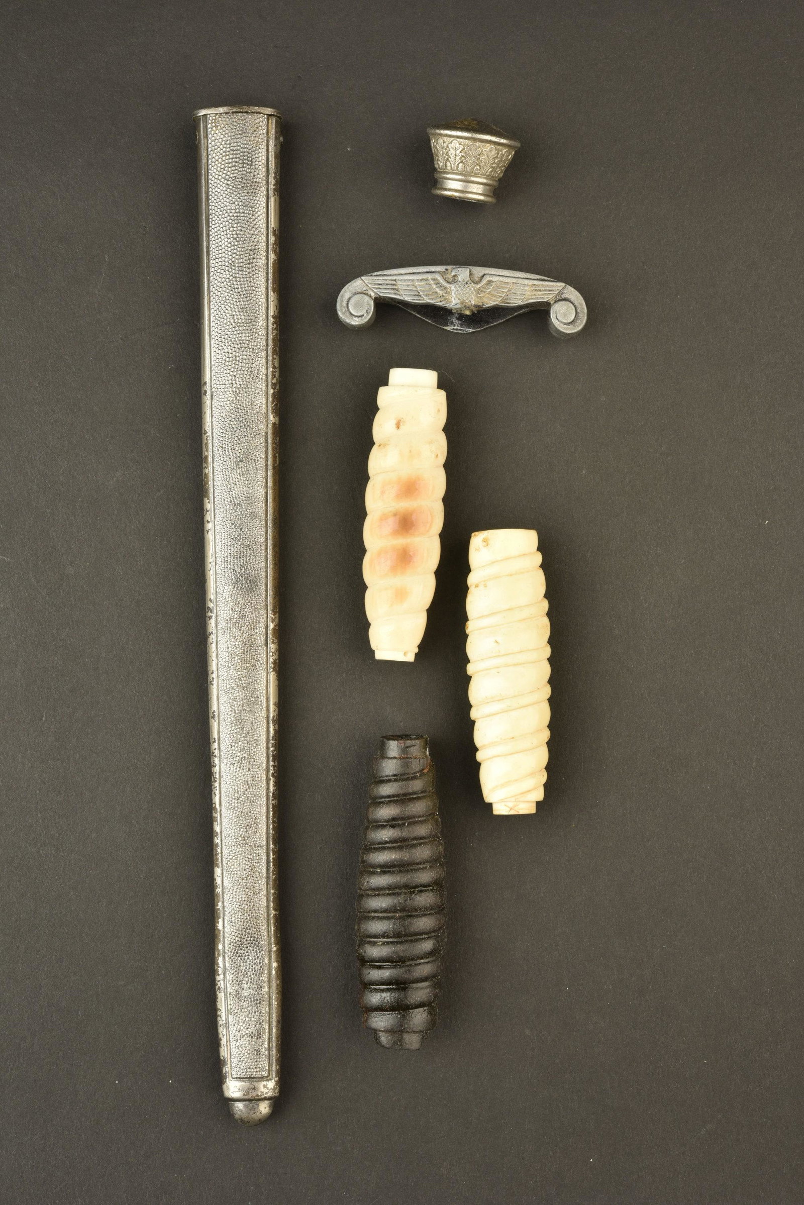 Accessoires de dague de la Heer. Heer dagger: Comprenant un fourreau en metal grenele, une vis manquante, nombreuses traces d oxydation. Deux fusees couleur blanche, une fusee couleur noire. Une garde denazifiee. Un pommeau. A noter une certaine 