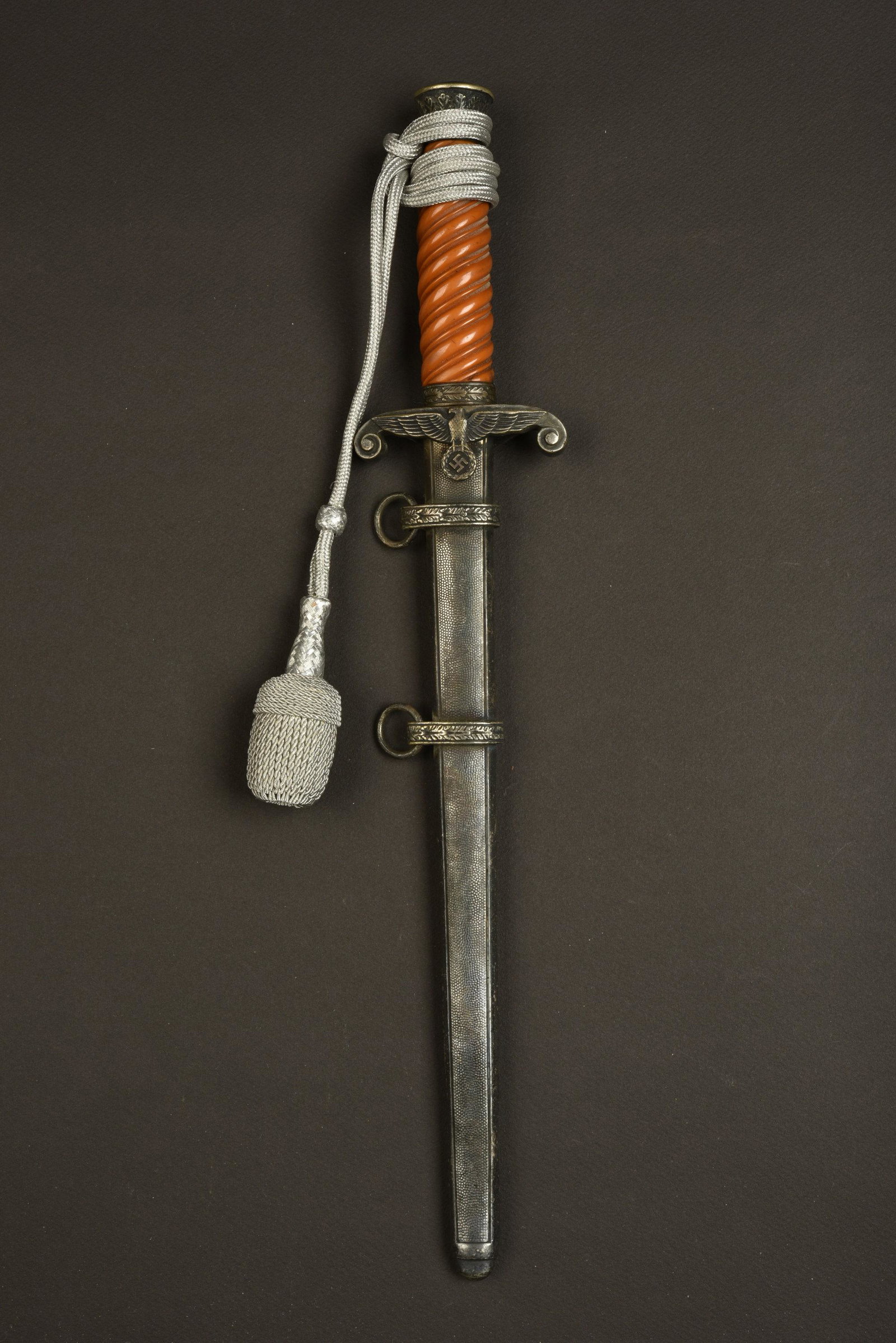 Dague d officier de la Heer. Heer officer dagger.: Poignee en matiere plastique orange foncee. Toutes les garnitures metalliques sont de couleur argent fonce. Dragonne en fil d argent presente. Lame usee presentant quelques taches et marques d oxydati