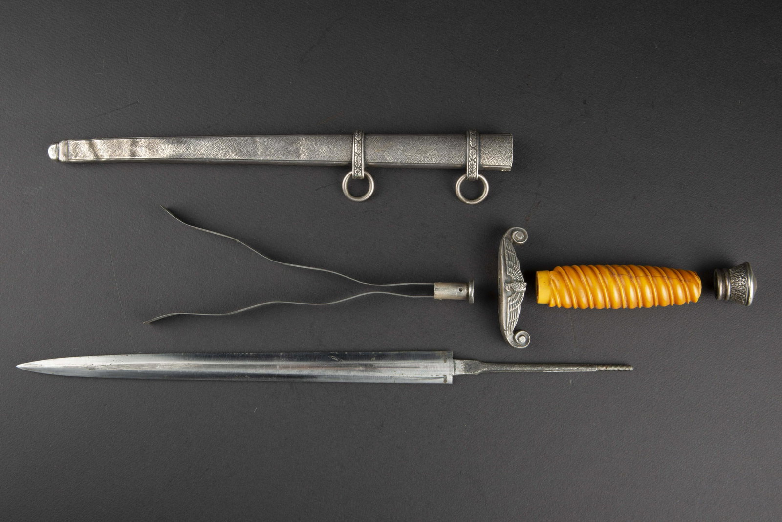 Piece detachee de dague Heer. Heer dagger spare part.: Comprenant une fusee orange, fendue. Une lame de dague fortement usee, reste de marquages WKC. Une garniture interieure de fourreau. Un fourreau en metal, bossele sur son dernier tiers. Une garde en m