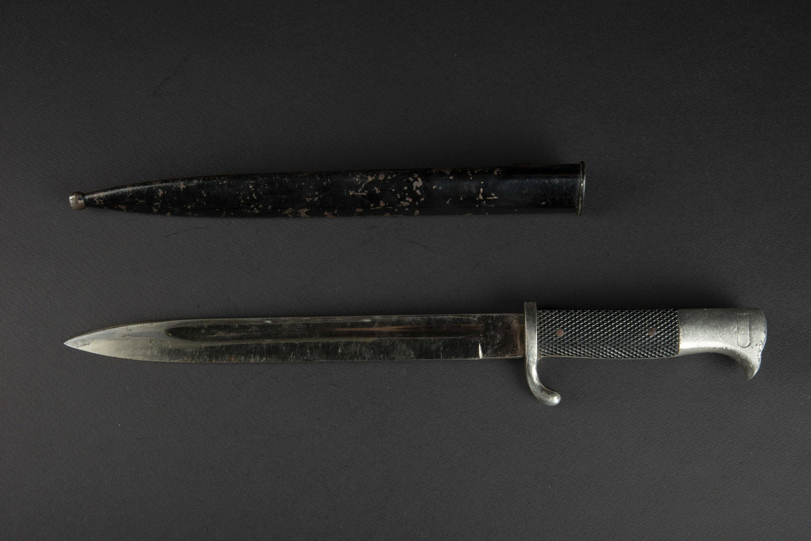Baionnette de sortie. German Bayonet.: Garnitures en metal nickele, fortement use. Plaquettes en bakelite noire grenelees. Lame complete dans sa longueur, couleur d origine Ã 70%. Fabrication WKC. Lame presentant un jeu. Fourreau en met