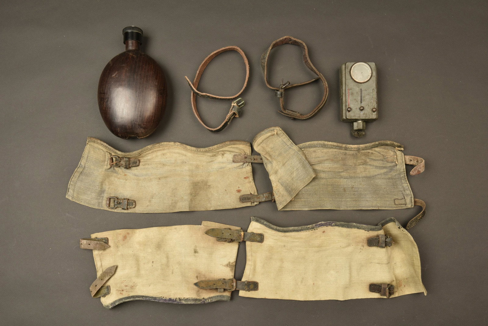 Ensemble d equipements allemands. Equipment set.: Comprenant une lampe de poche Daimon sans pile ni ampoule. Une gourde coco avec son bouchon en bakelite datee 1942. Une paire de guetres homogenes en toile feldgrau fortement delavee. Deux sangles en 