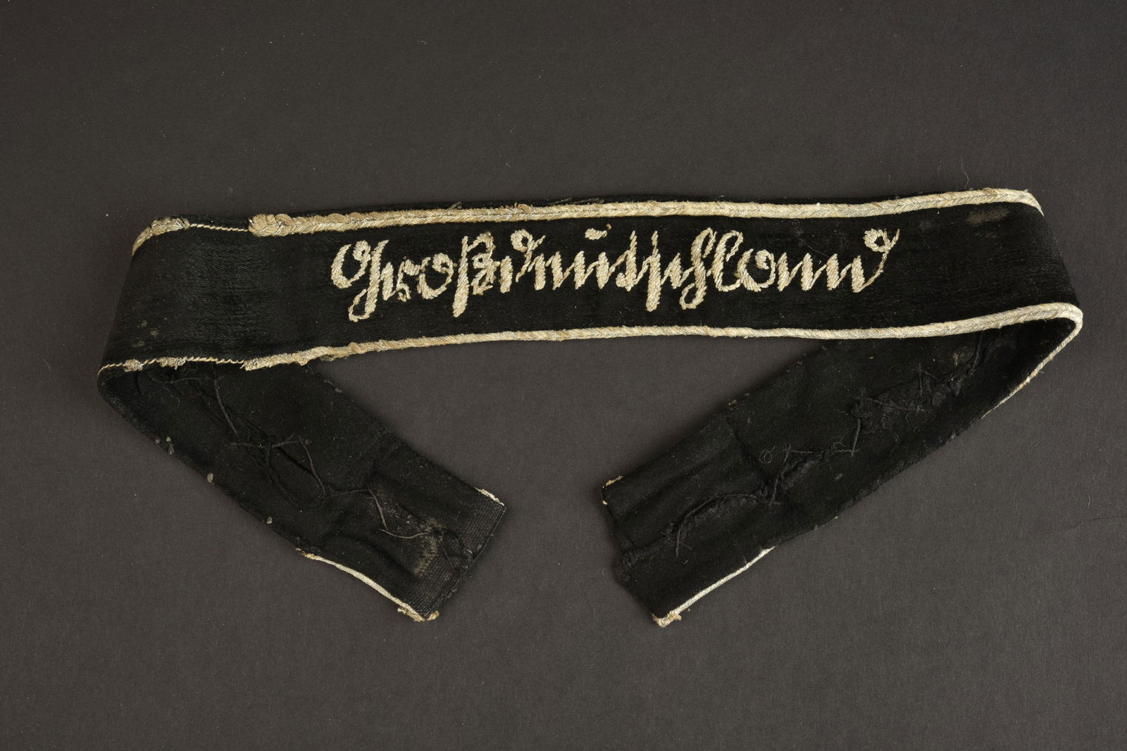 Bande de bras Grossdeutschland. Grossdeutschland cuff: En tissu type velours noir. Broderie en fil d argent. Deux galons argent incomplet sur les bordures. A noter une certaine usure et patine de la piece, ainsi que quelques manques et ta ches. Longueur 4