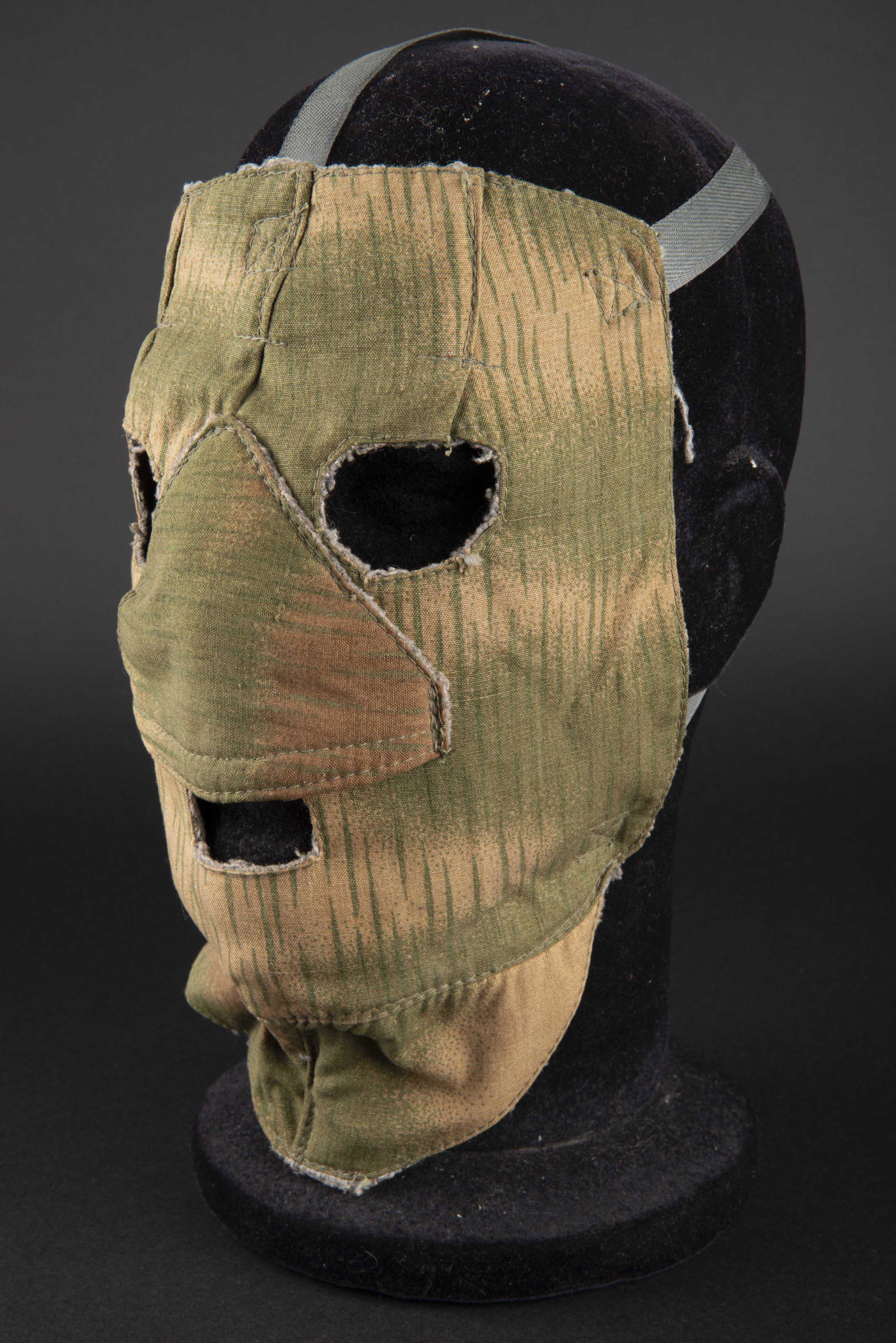 Masque facial camoufle. Camo face mask.: En toile camoufle flou. Tous les boutons sont presents, ainsi que toutes les sangles. Interieur double en epais drap gris. Sans marquages visibles. A noter une legere usure et patine de la piece. Masq