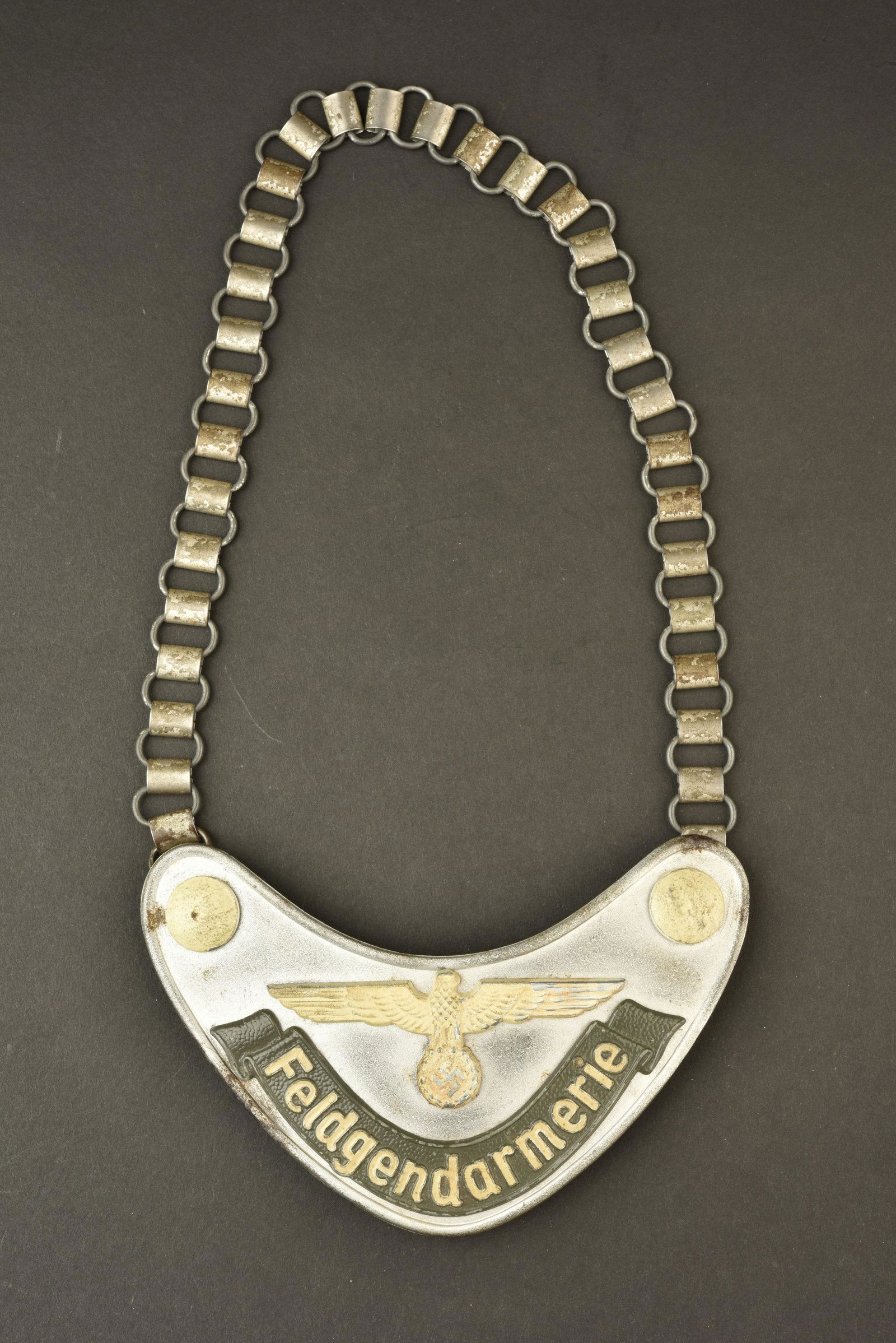 Hausse col Feldgendarmerie. Feldgendarmerie gorget.: En aluminium. l Aigle, les boutons, et la mention Feldgendarmerie sont phosphorescent. ChaÃ®nette complete. Doublure en drap Feldgrau, presentant des manques et des trous de mite, logo du fabricant