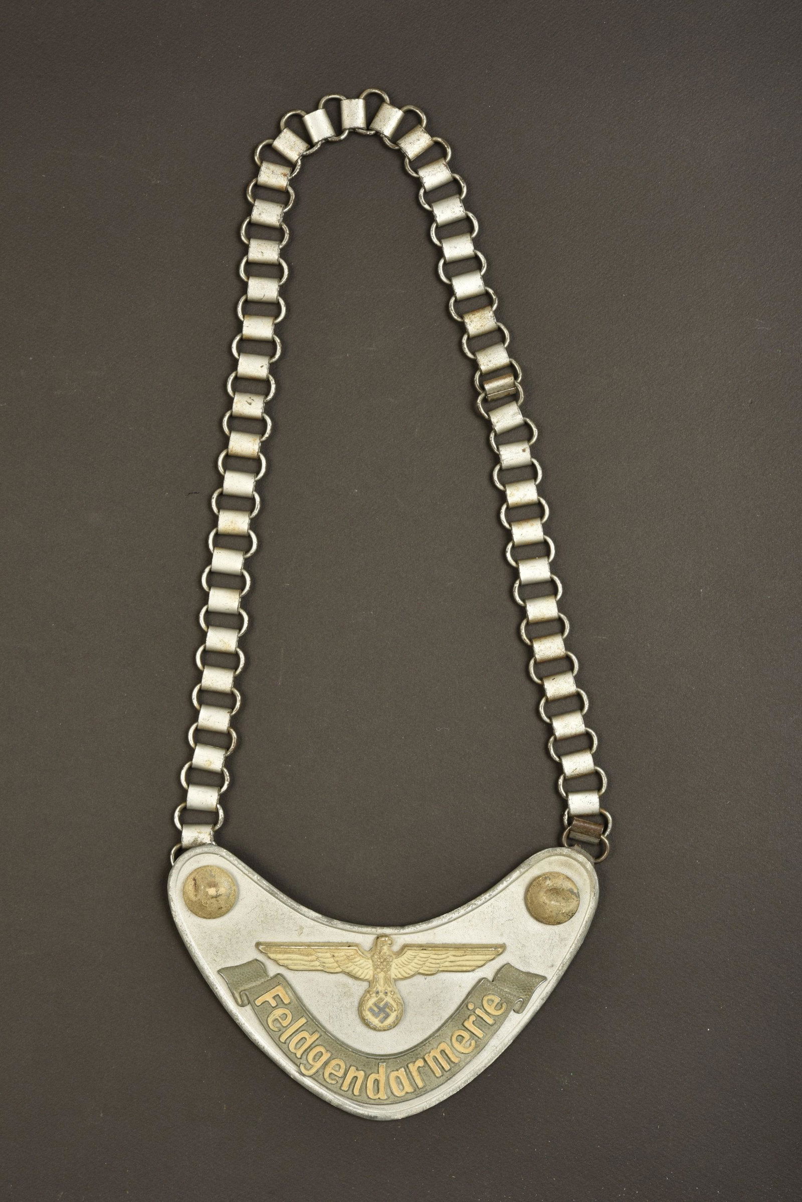 Hausse col Feldgendarmerie. Feldgendarmerie gorget.: En aluminium, une bosse sur un bouton. l aigle, les boutons, et la mention Feldgendarmerie sont phosphorescent. ChaÃ®nette complete. Doublure en drap Feldgrau, reste de marquages illisibles. Patte d