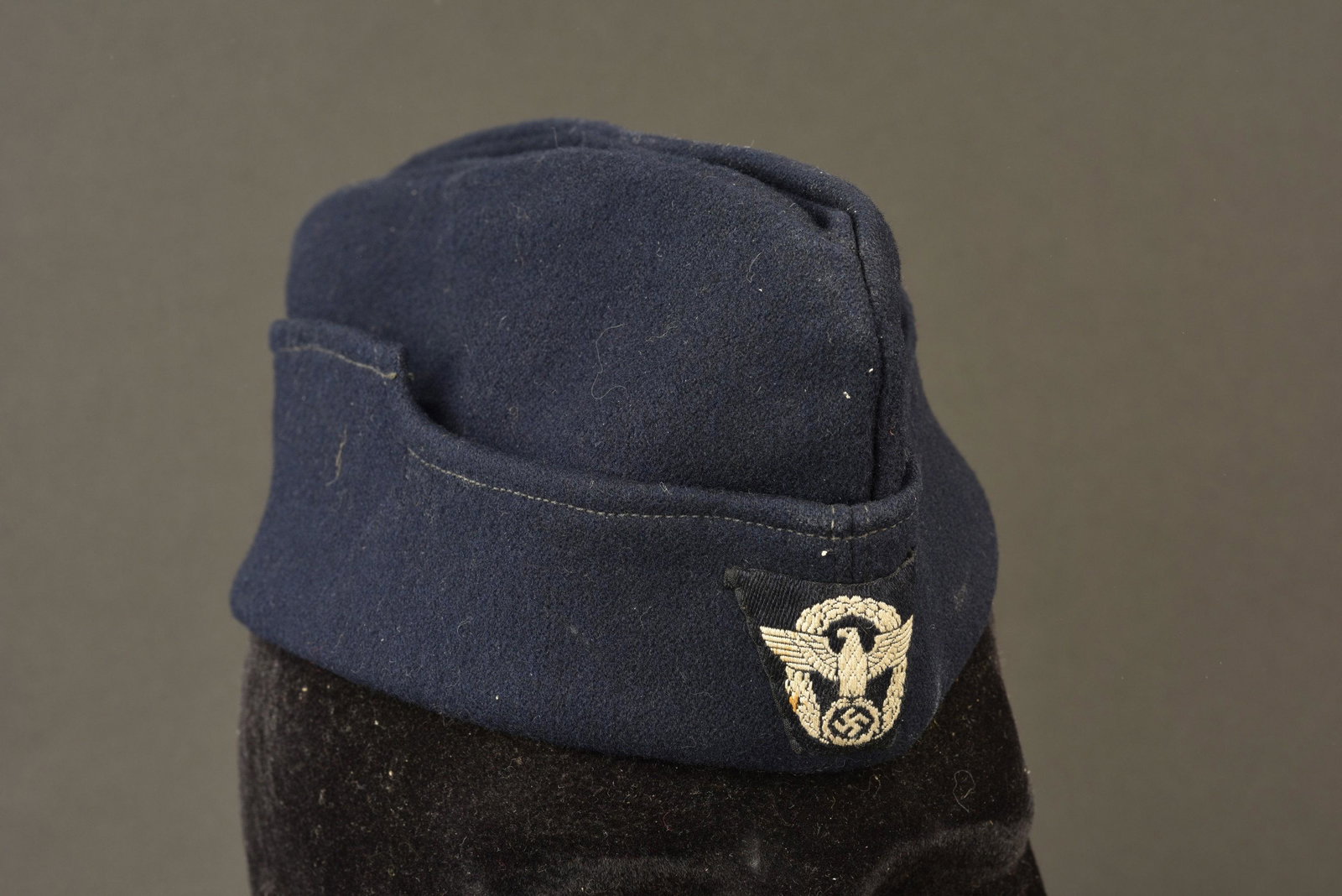 Calot de la police municipale. Municipal police cap.: En drap bleu marine, insigne de la Police Bevo, monte main. Interieur double en tissu coton blanc, sans marquages visibles. A noter une certaine usure et patine de la piece, ainsi que quelques traces 
