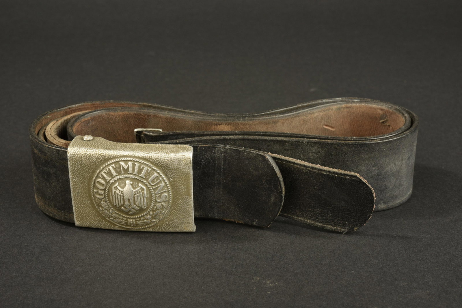 Ceinturon de la Heer. Heer belt.: Ceinturon en cuir noir, bouclerie en metal. Taille 105. Marquages illisibles. Boucle de ceinturon en aluminium grenele, patte en cuir datee 1939. A noter une certaine usure et patine de la piece. Plus