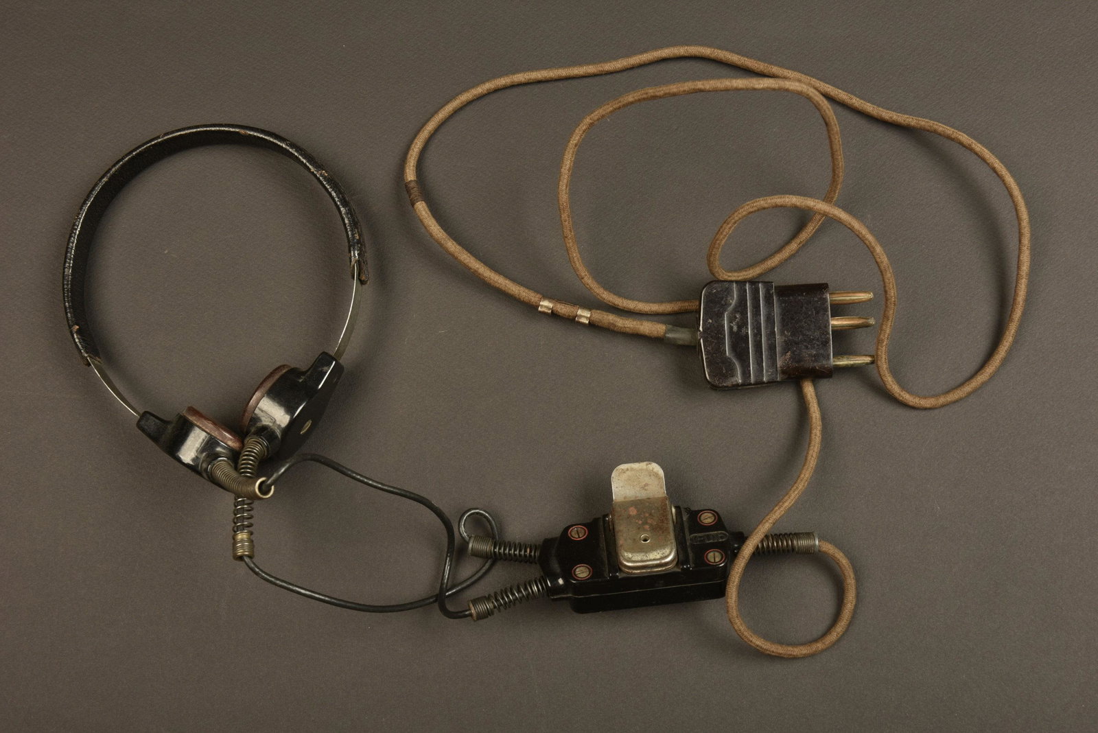 Laryngophone allemand. German laryngophone.: Armature metallique recouverte de cuir noir. Laryngophone en bakelite marron. Ca ble et prise presents. Interrupteurs complet avec sa pince de fixation. A noter une certaine usure et patine de la piec