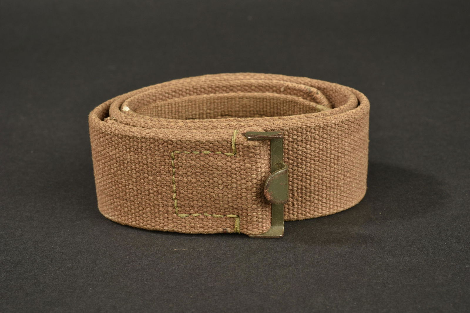 Ceinturon tropical AK. AK tropical belt.: En toile sable, bouclerie en metal peint. Taille 85. Marquages presents, mais illisibles. A noter une certaine usure et patine de la piece. Plus de photos sur www.aiolfi.com. In sand canvas, painted m