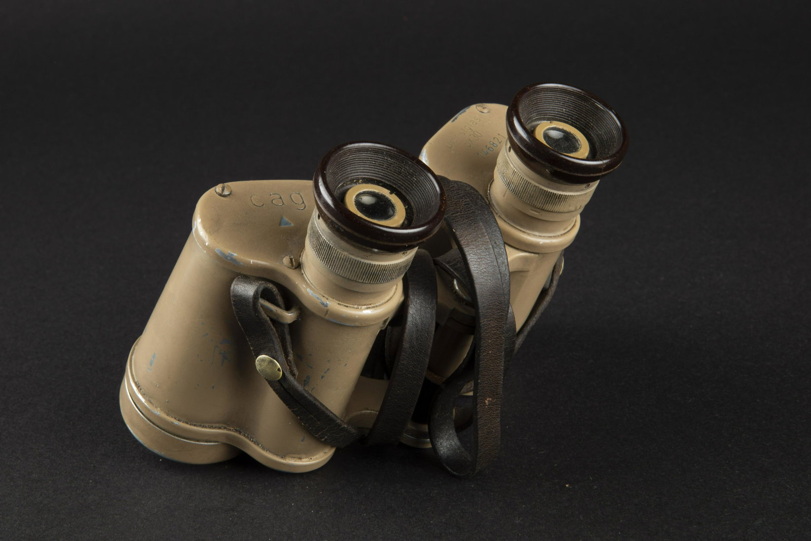 Jumelles 6x 30. 6X30 binocular.: En metal, couleur sable a 90%, revetement lisse. Oculaire en bakelite marron. Une felure sur un oculaire. Marquages CAG Dienstglass 6x30 146821, triangle bleu present. Optiques claires. Sangle de tran