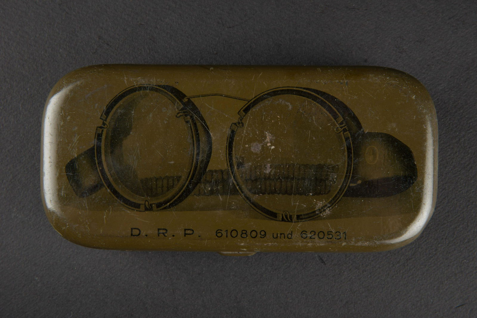Lunette de vol LW en boite. LW flight glasses in box.: Boite en metal, peinture a 90%. Couvercle bien marque DRP 610809 und 620531. Armature en bakelite et metal, verres blanc. Elastique souple. Reste d etiquette marquee Auf den Bugel Drucken. A noter une