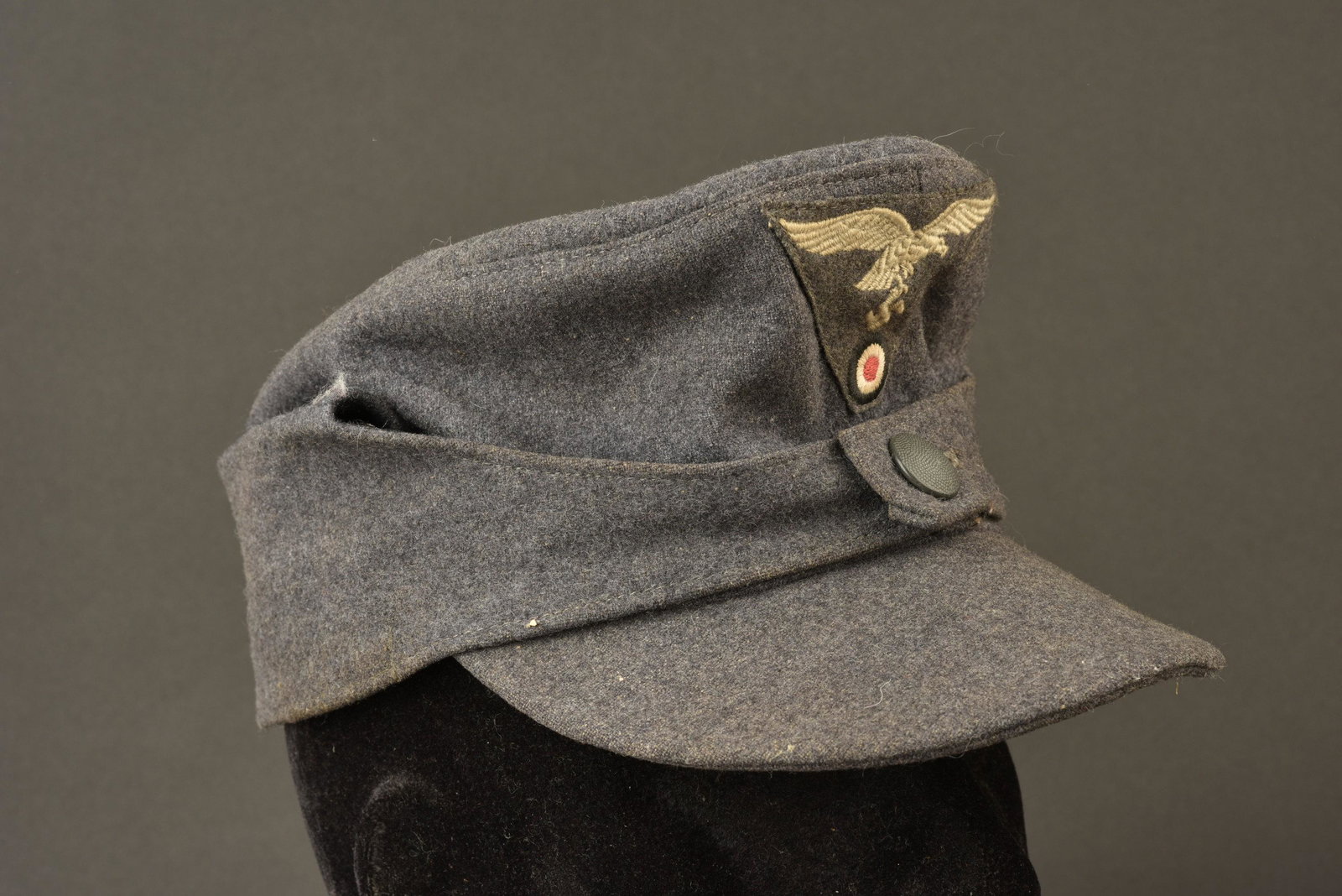 Casquette M43 LW. Luftwaffe M43 cap.: En drap gris bleu. Un seul bouton fermant le rabat, celui ci est en couleur d origine. Aigle et cocarde brodes sur fond gris bleu, montage machine. Visiere complete, pas de trace de cassure au niveau 