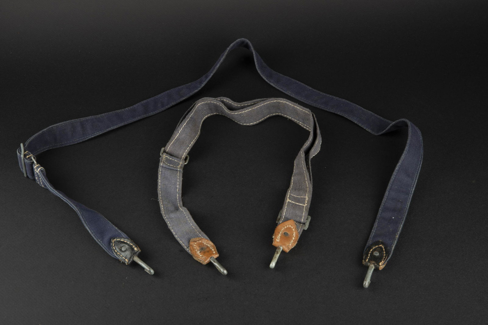 Sangles de sac a pain LW. LW bread bag straps.: Comprenant une sangle en tissu gris bleu, les mousquetons sont complets, cuir fauve, sans marquages visibles. Une sangle en tissu bleu fonce, cuir noir, les mousquetons sont presents. Sans marquages v