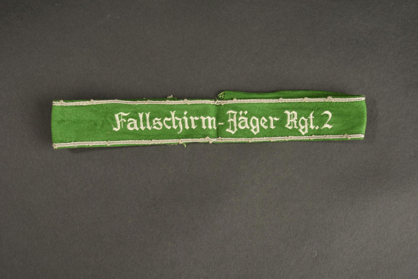 Bande de bras FallschirmjÃ¤ger Rgt 2. FJR2 armband.: En tissus coton vert. Complete dans sa longueur, visiblement demontee d une vareuse. Double lisere en coton blanc. Broderie en fils blanc Fallschirm JÃ¤ger Rgt 2, lettrage gothique. A noter une cert