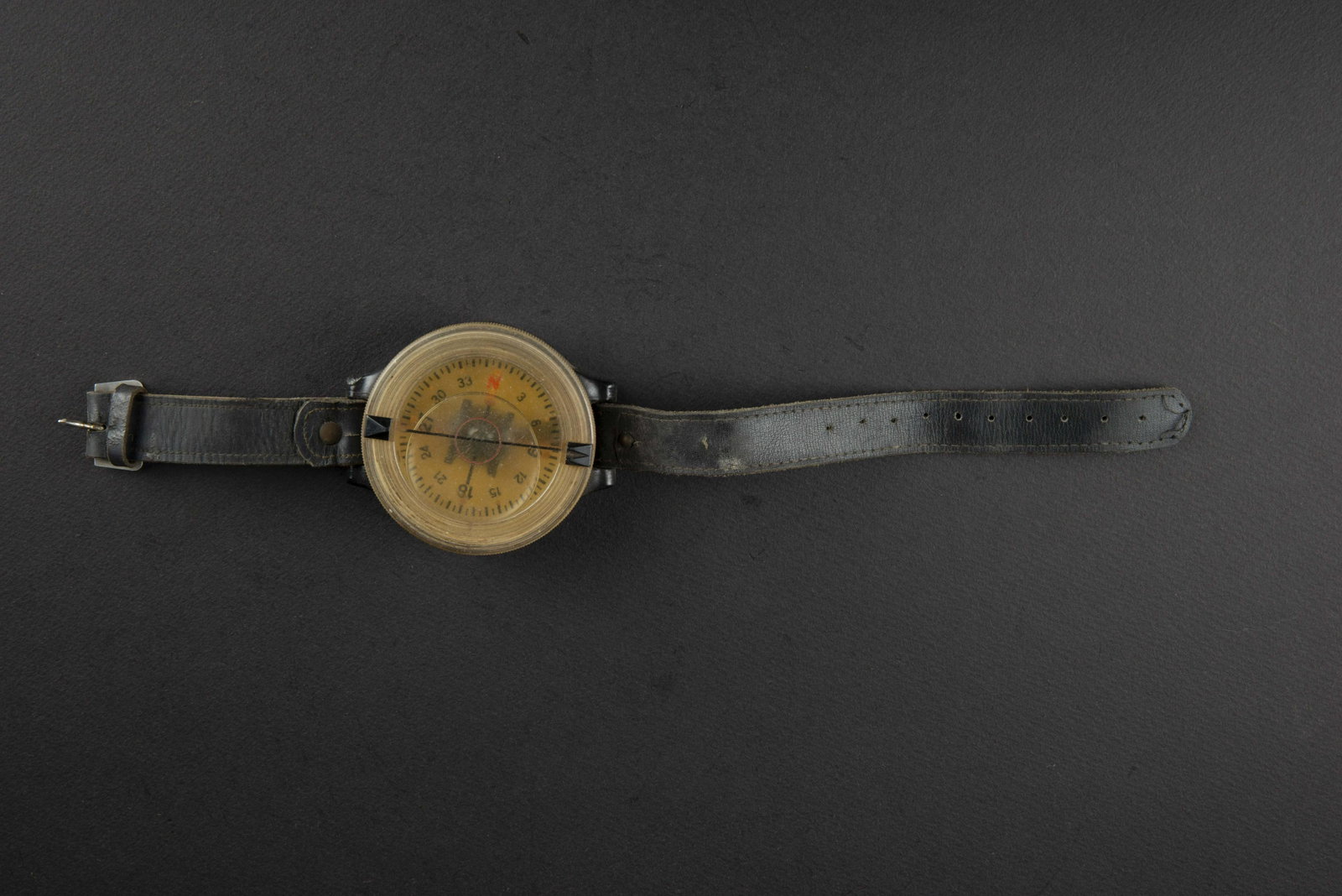 Boussole de poignee LW. LW handle compass.: Boitier en bakelite, fond blanc, liquide present. Fonctionnelle. Bracelet en cuir noir et bouclerie a ardillon en aluminium. Marquages AK 39 FL 23235 1. A noter une certaine usure et patine de la piec