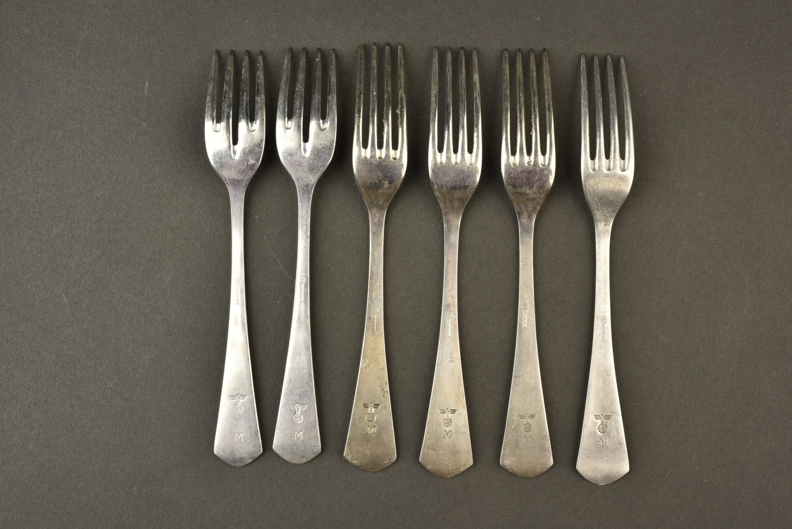 Petites fourchettes KM. Small forks Kriegsmarine.: Six petites fourchettes en metal, bien marquees Rostfrei. Insigne KM present. Deux modeles differents. A noter une certaine usure et patine des pieces. Cette piece provient du depÃ´t de materiel de 