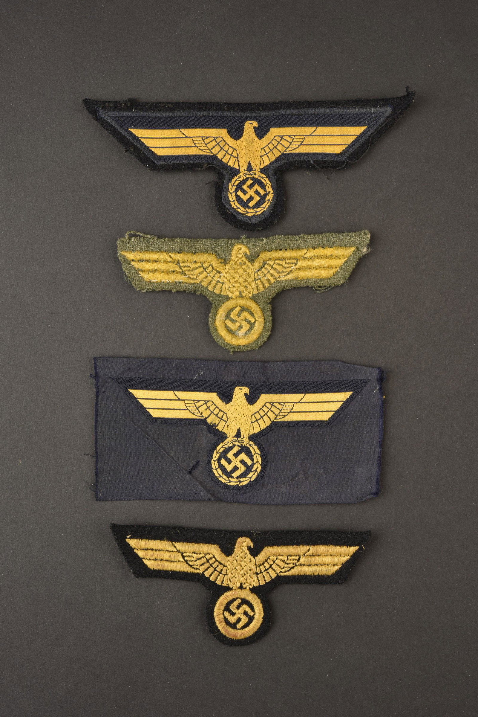 Ensemble aigles poitrine KM. Set eagles breast: Comprenant un aigle Bevo jamais monte, dos de la piece presentant de traces de col. Un aigle de poitrine Bevo monte sur drap bleu marine, visiblement demonte d une vareuse. Un aigle de poitrine brode 