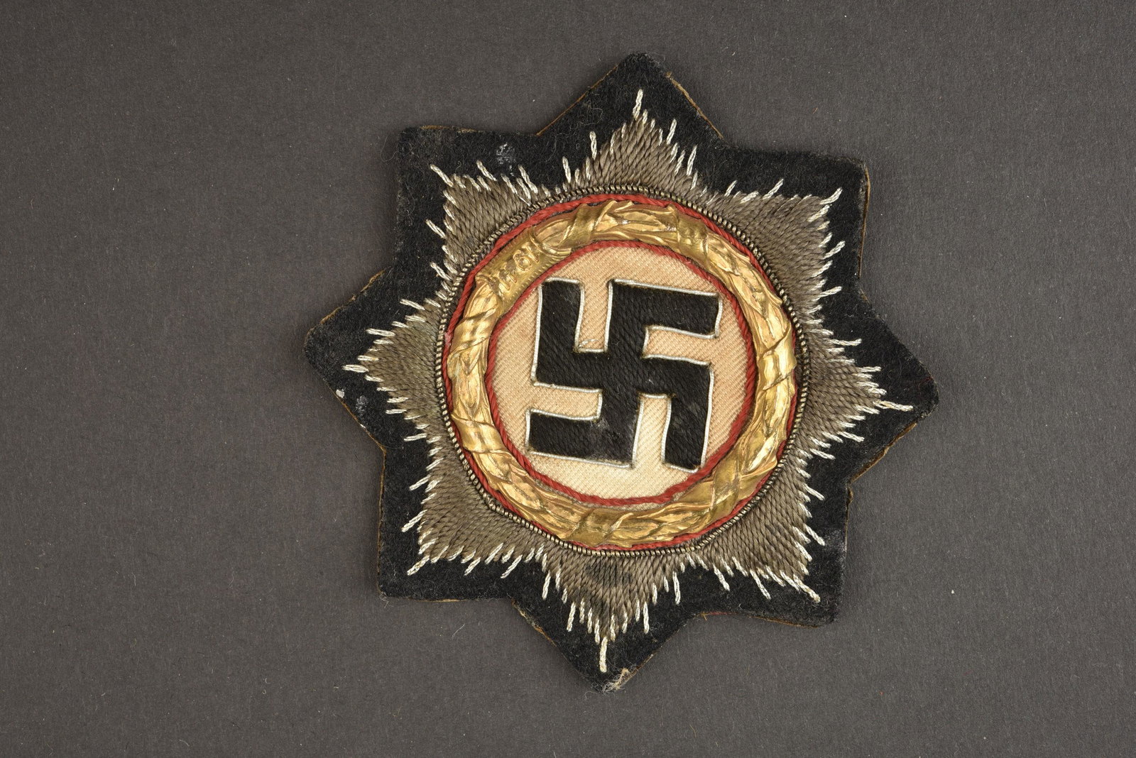 Deutsche Kreuz in Gold.: Modele brode sur fond bleu marine. Couronne de feuille de chene en metal dore. Dos de la piece double en papier cartonne. A noter une certaine usure et patine de la piece. Plus de photos sur www.aiolf