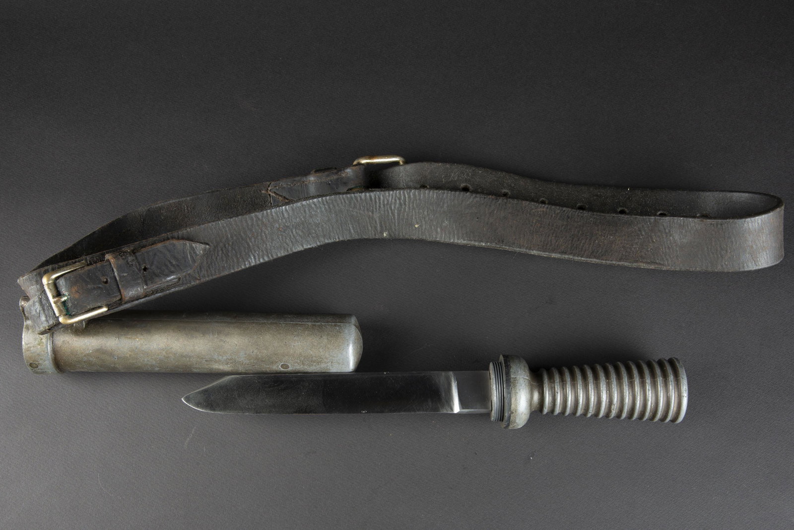 Couteau pied lourd. Heavy foot knife.: Manche en alliage de metal. Vis du pommeau en laiton. Traces de demontage. Joint en caoutchouc refait, trace de decoupe sur la bordure. Lame a un seul tranchant moderne et en parfait etat. Fourreau en