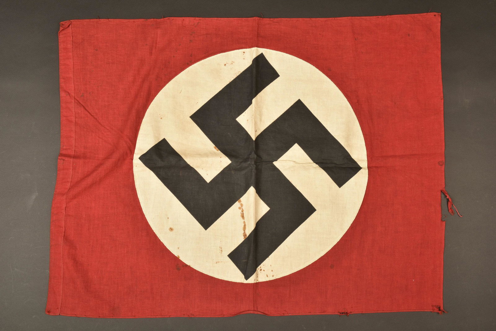 Drapeau allemand. German flag.: En tissu coton rouge, insigne national imprime et rapporte. Biface. Dimensions 57 x 75 cm. A noter une certaine usure et patine de la piece, ainsi que quelques taches, accrocs et manques. Plus de phot