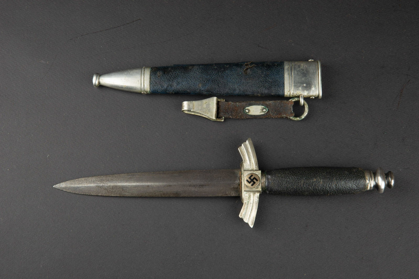Dague NSFK. NSFK dagger.: Garnitures en metal nickelees. Poignee en maroquin bleu. Couleur noir des insignes nationaux, present a 80 et 90%. Lame affÃ»tee et oxydee. Fabrication Gebr Heller Marienthal Schweina THR. Fourreau 