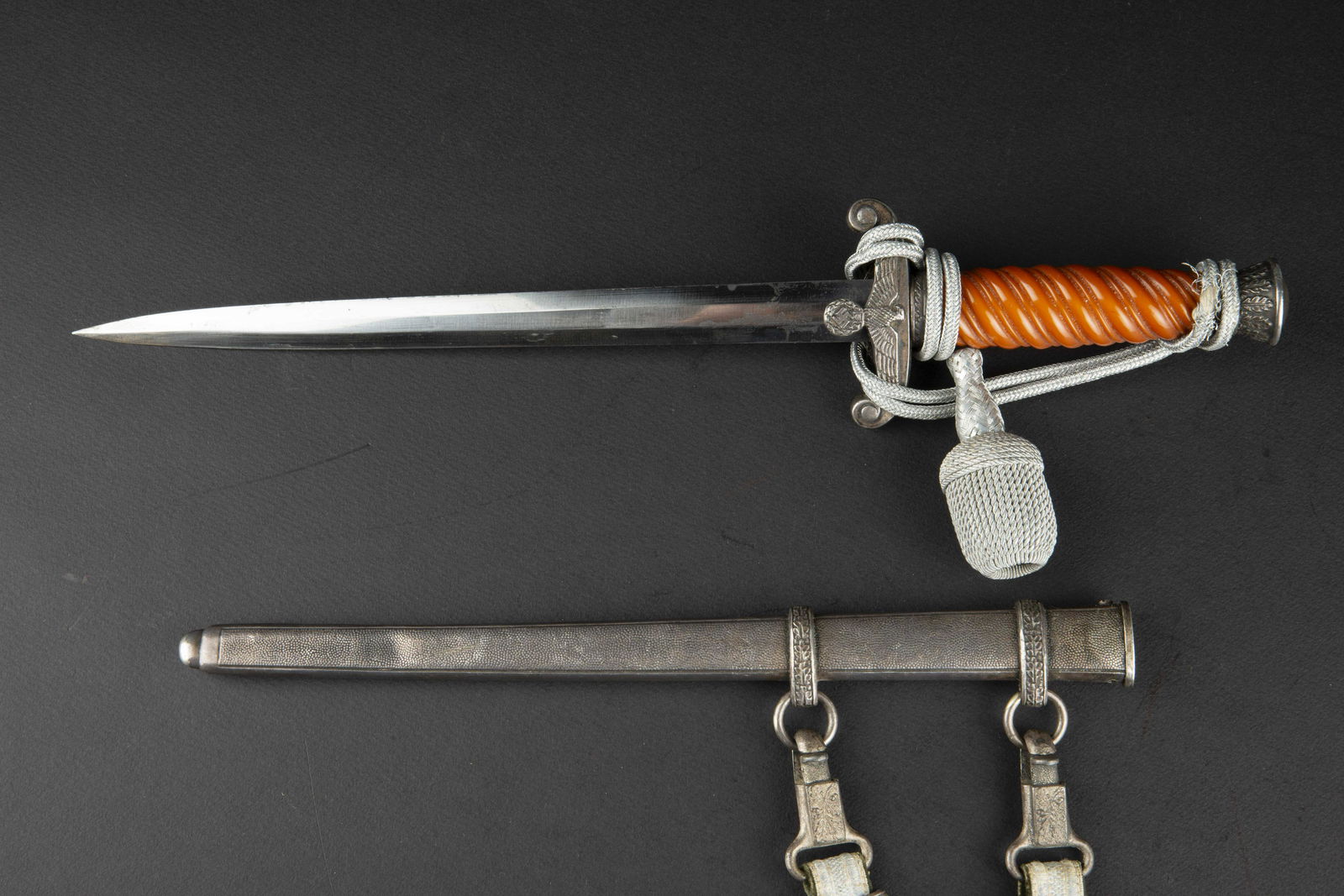 Dague d officier de la Heer. German Dagger.: Dague d officier de la Heer. Garnitures en metal, couleur argent. Fusee de couleur orange fonce. Dragonne en fil d argent monte de maniere reglementaire, effilochee. Fourreau en metal grenele, bagues