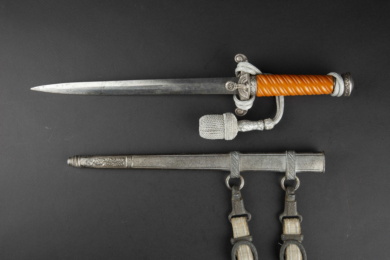 Dague d officier de la Heer. German Dagger.: Dague d officier de la Heer. Garnitures en metal, couleur argent. Fusee de couleur orange. Dragonne en fil d argent monte de maniere reglementaire. Fourreau en metal grenele, bagues decorees de feuill