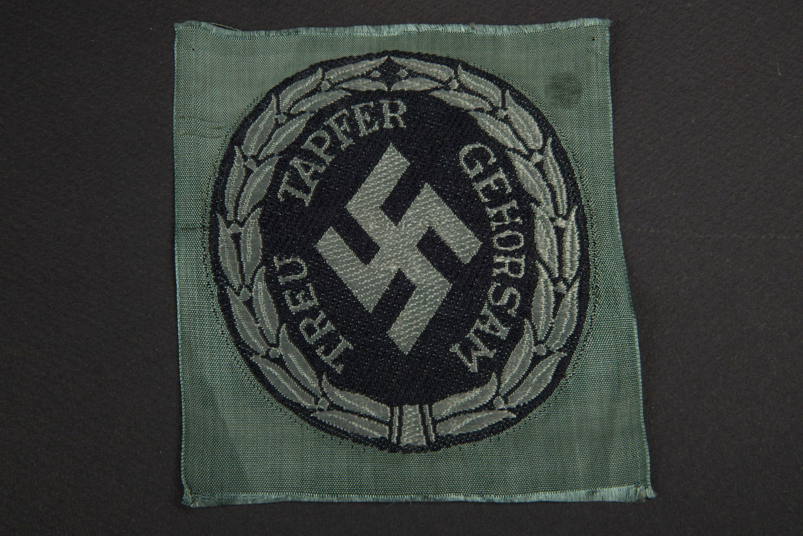 Insigne de bras Schuma. Schuma arm insignia.: Insigne tisse Bevo, jamais monte. Insigne national et mentions Treu Tapfer Gehorsam. A noter une legere usure de la piece. Plus de photos sur aiolfi.com. Bevo woven badge, never mounted. National badg