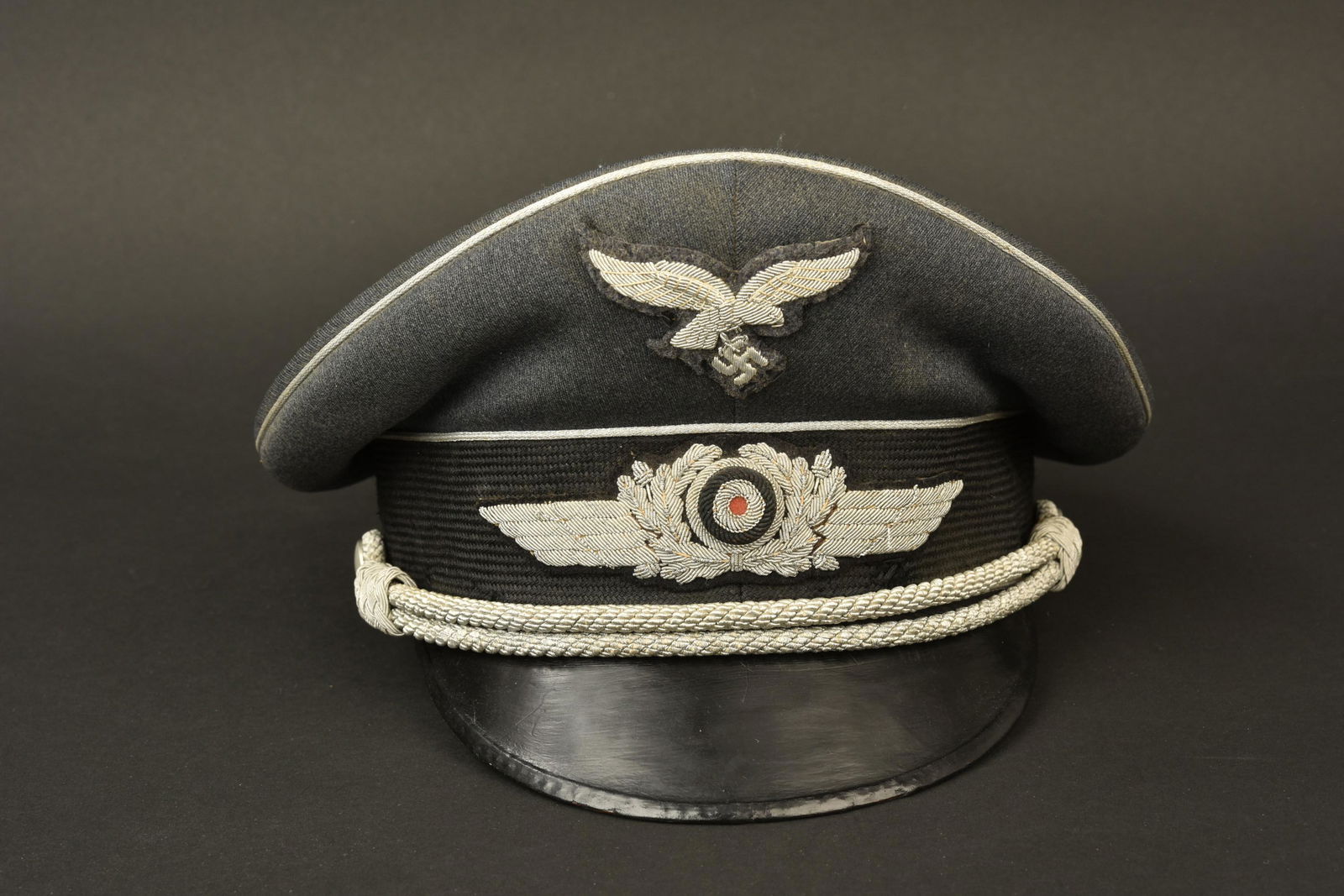 Casquette officier LW. Lufwaffe cap: Casquette d officier de la Luftwaffe. En gabardine gris/bleu. Triple lisere argent. Insignes en cannetille argent. L aigle est remonte posterieurement. Fausse jugulaire d officier presente. Interieur